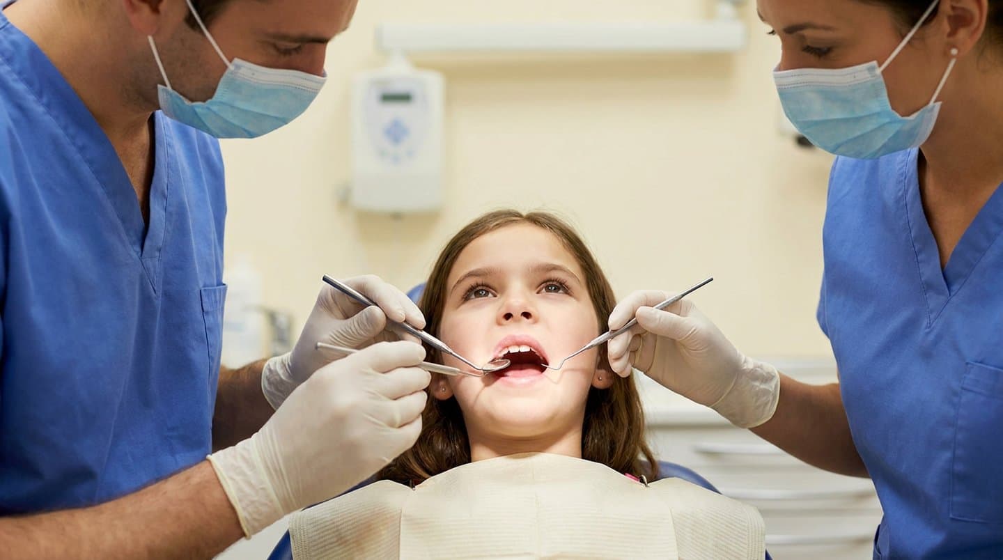 A calm child in a dental chair during an exam while clinicians use a mirror and explorer