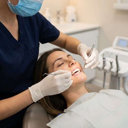 Clinician using dental instruments during a hygiene visit while the patient relaxes in the chair