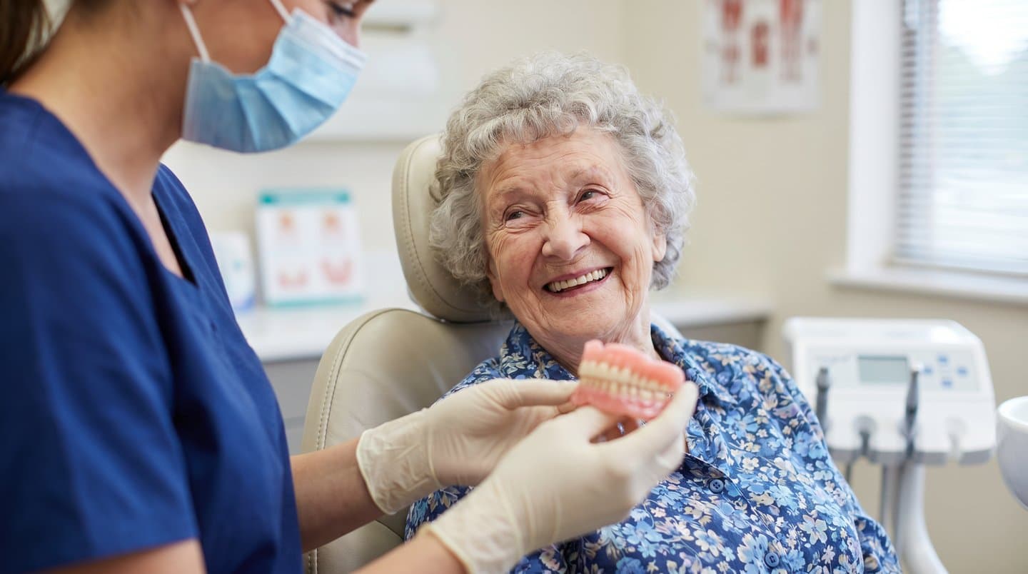 A dental professional showing a denture to a smiling patient seated in a dental chair