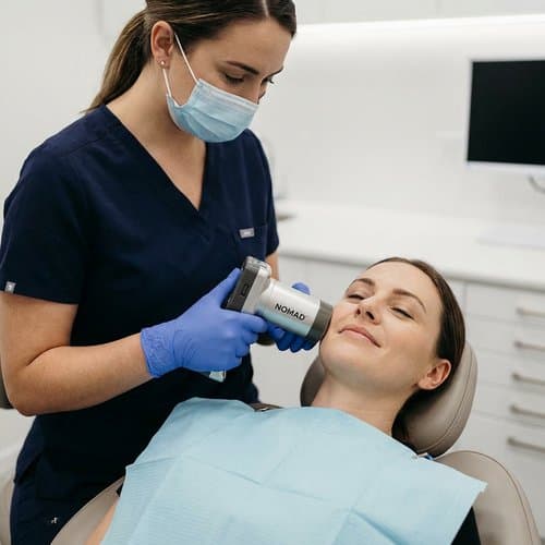 Clinician using a Nomad handheld dental X-ray with a relaxed patient in the chair